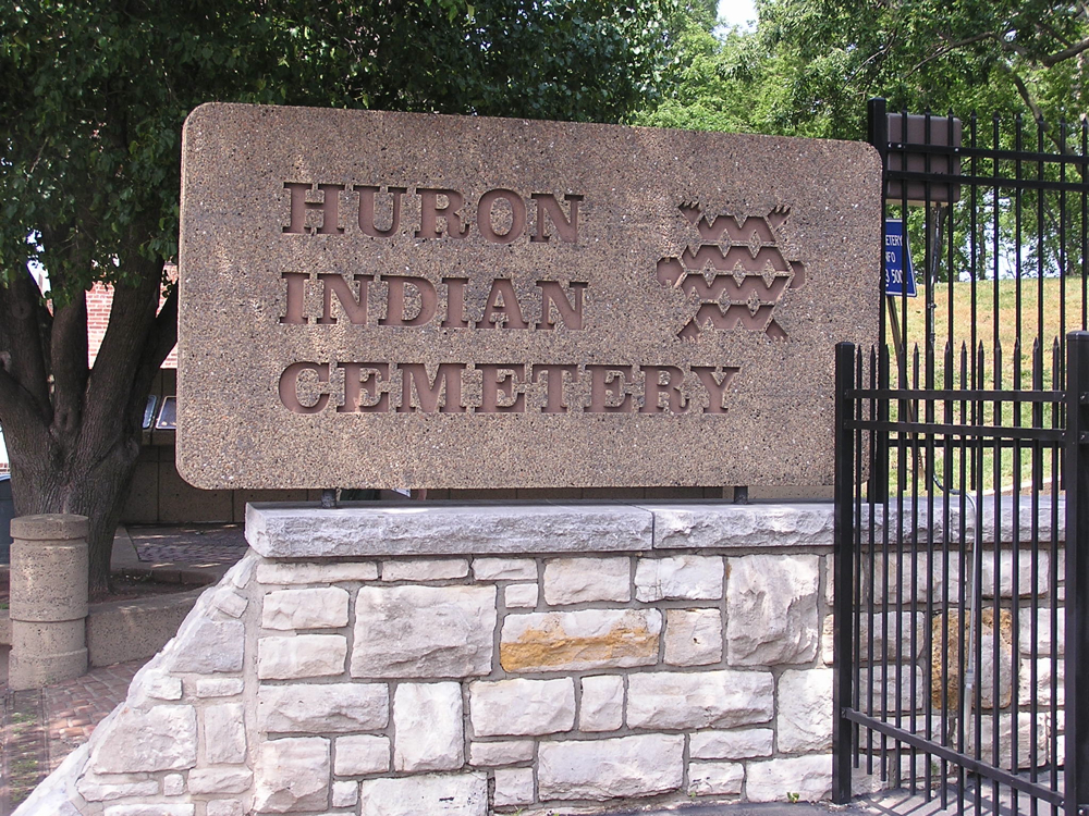 Photo of the entrance to the Wyandot National Burying Ground. A large brown marble stone with "Huron Indian Cemetery" and and artistic turtle cared into it sits on a square stone wall. Photo by Mark Michalovic